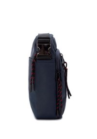 Bolso azul marino con un diseño elegante, tejido texturizado, herrajes brillantes, correa ajustable y cuerdas de acento en rojo y negro. Vista lateral.