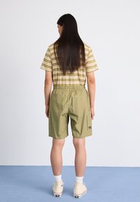Pantalones cortos caqui con cinturilla elástica, dos bolsillos laterales y un bolsillo trasero, combinados con una camiseta de manga corta a rayas en amarillo y verde.