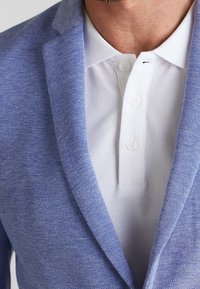 Light blue textured blazer with notched lapels over a white polo shirt featuring three buttons and a flat collar.
