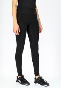 Zwarte sportlegging met een hoge tailleband, voorzien van platte naden en een aansluitend ontwerp. Gecombineerd met zwarte sneakers, met minimale details.