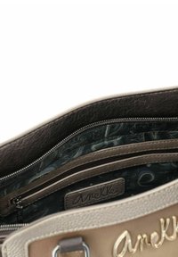 Beige Handtasche mit einer strukturierten Lederaußenseite, ausgestattet mit einem dunkel gemusterten Innenfutter und einer Reißverschlusstasche. Geprägtes Logo im Inneren.