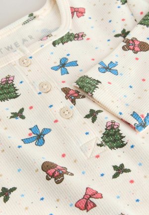 Bomullsoverall i krämfärg med texturerad ribbad tyg, prydd med färgglada tryck av träd, rosetter och pepparkaksgubbar. Tre knappar vid halsen.
