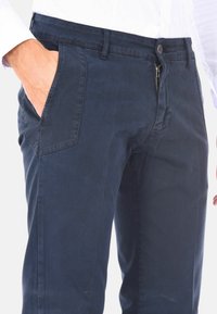 Chino in cotone blu navy con zip e chiusura a bottone, dotato di tasche laterali e design a gamba dritta. Texture liscia e design semplice.