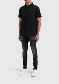 Zwarte polo met een drie-knopenblik, gecombineerd met donkergrijze jeans en witte sneakers. Gladde textuur en een strakke pasvorm.