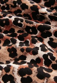 Tkanina s uzorkom leoparda koja sadrži crne i smeđe mrlje na bež pozadini, s teksturiranom površinom i mekim padanjem.