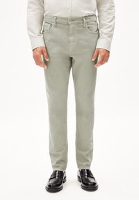 Pantalons en coton vert clair à coupe slim, design à cinq poches et fermeture à bouton. Associés à des chaussures en cuir noires.