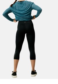 Svarta capribyxor med reflekterande detaljer och hög midja, tillsammans med en blå långärmad topp, sedd bakifrån.