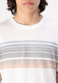 Weißes T-Shirt mit kurzen Ärmeln, das horizontale Streifen in Blau, Schwarz und Orange zeigt. Weicher Stoff mit subtiler Struktur. Logo am Saum.