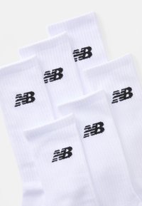 White cotton socks in a ribbed texture featuring a black embroidered New Balance logo on each sock. Six pairs shown.