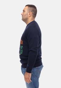 Granatowy sweter z okrągłym dekoltem, ozdobiony kolorowymi nadrukami przedstawiającymi słońce i butelkę z przodu, zestawiony z niebieskimi dżinsami.