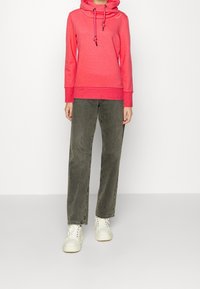 Felpa rosa con collo a giro, cordini e polsini a coste abbinata a jeans verde oliva a vita alta e gamba larga, e sneakers bianche.