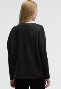 Schwarzer, langärmeliger Pullover mit lässigem Schnitt. Weiche Textur und runder Ausschnitt. Mit abgesenkten Schultern und geradem Saum.