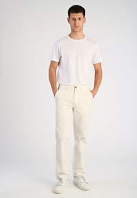 T-shirt bianca abbinata a chinos beige chiaro. L'outfit presenta una vestibilità classica, un tessuto morbido e sneakers bianche per un look casual.