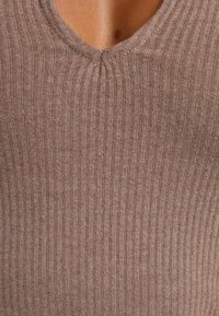 Brun ribbad topp med V-ringning, som har en mjuk textur och subtila variationer i tyget, vilket betonar en figurnära design.