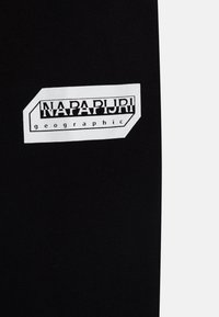 Schwarzer Stoff mit einem weißen rechteckigen Logo-Patch, auf dem in fetter Schrift "NAPAPIJRI" und "geographic" steht.