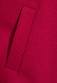 Tejido rojo con una textura suave que presenta un bolsillo rectangular cosido en la superficie, mostrando un diseño simple y un color vibrante.