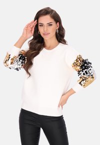 Witte trui met lange mouwen en details van gouden, zwarte en zilveren pailletten. Regular fit en geribbelde manchetten, gestyled met zwarte broek.