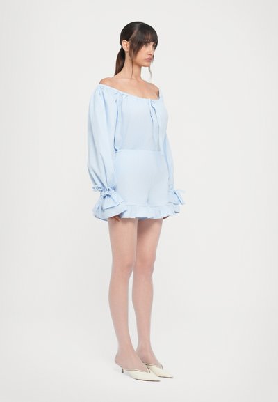 Combi-short bleu clair à épaules dénudées avec des manches longues, des accents volants et une taille cintrée. Tissu lisse avec une texture douce.
