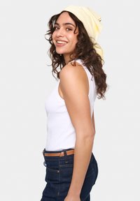 Fehér ujjatlan felső, sötétkék farmerral és barna övvel viselve. Haja sárga csíkos fejkendőben van feltűzve, természetes göndör textúrával.