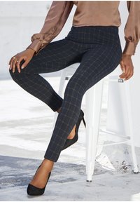 Marine-karierte Leggings mit goldenen Linien, enganliegendem Design und seitlichen Schlitzen, kombiniert mit schwarzen High Heels. Glatte Stoffstruktur ist deutlich sichtbar.