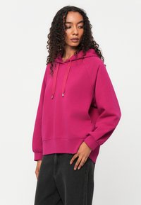 Fuchsia Kapuzenpullover mit Kängurutasche, gerippten Bündchen und verstellbaren Zugbändern. Mit einem lockeren Schnitt und weichem, strukturiertem Stoff.