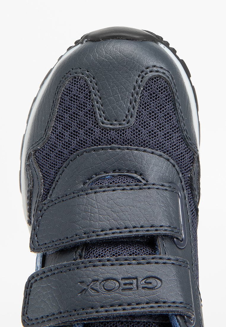 Granatowe trampki z ciemnej skóry i siateczki, z dwoma paskami na rzepy. Okrągły czubek i teksturowana gumowa podeszwa. Widoczne logo Geox.
