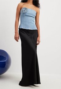 Top senza spalline in denim con dettaglio a rosa, abbinato a una gonna nera in satin slim. Texture liscia, design aderente e colori a contrasto.