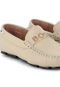 Beige ādas loafers ar izšūtu "BOSS" logo, šūšanas detaļām un melnu gumijas zoli. Gluda virsma ar viegli uzvelkamu dizainu.