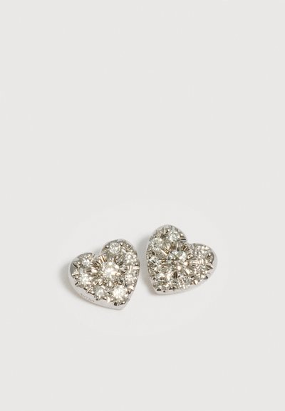 Boucles d'oreilles en argent en forme de cœur incrustées de plusieurs petites pierres précieuses claires et scintillantes sur un fond clair uni.