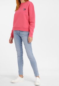 Sweat-shirt rose avec un col rond et des poignets côtelés, associé à un jean skinny bleu clair et des baskets blanches. Présente un petit détail de logo.