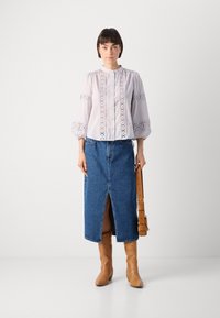 Gaismas lavandas blūze ar mežģīņu detaļām, apvienota ar garu džinsu svārku ar priekšējo izgriezumu. Brūni ādas augstpapēžu zābaki līdz ceļiem pabeidz kopskatu.