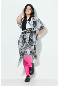 Un abito oversize a fantasia bianco e nero con un design drappeggiato, abbinato a leggings rosa acceso e scarpe nere chunky.