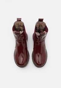 Bottines en cuir bordeaux avec une finition lisse, doublure en fausse fourrure et languettes de tirage. Bout légèrement arrondi et semelle en caoutchouc texturée.