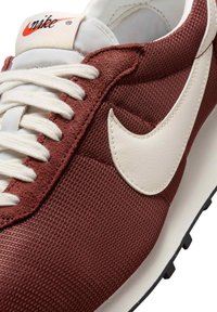 Sapatilha de tecido vermelho com detalhes em couro branco. Apresenta atacadores redondos e um destacado logótipo Nike swoosh branco. Sola leve com solas pretas.