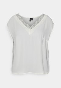 Hvid ærmeløs bluse med V-udskæring, der er kantet med delikat hvid blonde, præsenteret mod en ensfarvet baggrund.