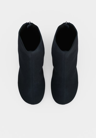 Paire de bottines noires à finition lisse, vue de dessus sur un fond clair uni.