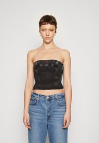 Top senza spalline in denim nero con design aderente, cuciture a vista e un piccolo dettaglio con logo rosso. Abbinato a jeans chiari a vita alta.