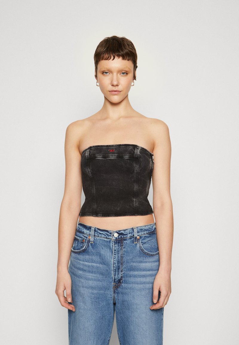 Top senza spalline in denim nero con design aderente, cuciture a vista e un piccolo dettaglio con logo rosso. Abbinato a jeans chiari a vita alta.