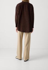 Camicia marrone con una vestibilità rilassata, maniche lunghe e polsini con bottoni. Abbinata a pantaloni a gamba larga color crema e calzature neutre.