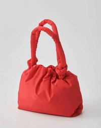 Borsa in tessuto rosso con parte superiore arricciata, dotata di due manici annodati. Texture liscia, forma morbida e design capiente.