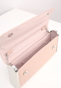 Obdélníková světle růžová kabelka do ruky s otevřenou klopou, stříbrnými kovovými okraji, vnitřní kapsou na zip a magnetickým zapínáním na bílém povrchu.