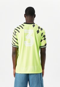 Zöld sportmez fekete csíkos ujjakkal, a hátsó oldalon a "3" szám látható. Simább, könnyű anyagból készült.