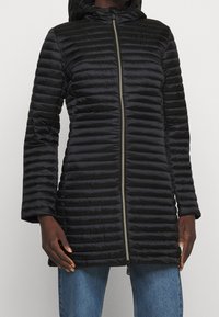 Schwarze Steppjacke mit Kapuze, ausgestattet mit einem Reißverschluss auf der Vorderseite, geripptem Material und langen Ärmeln. Das Material wirkt glatt und leicht.