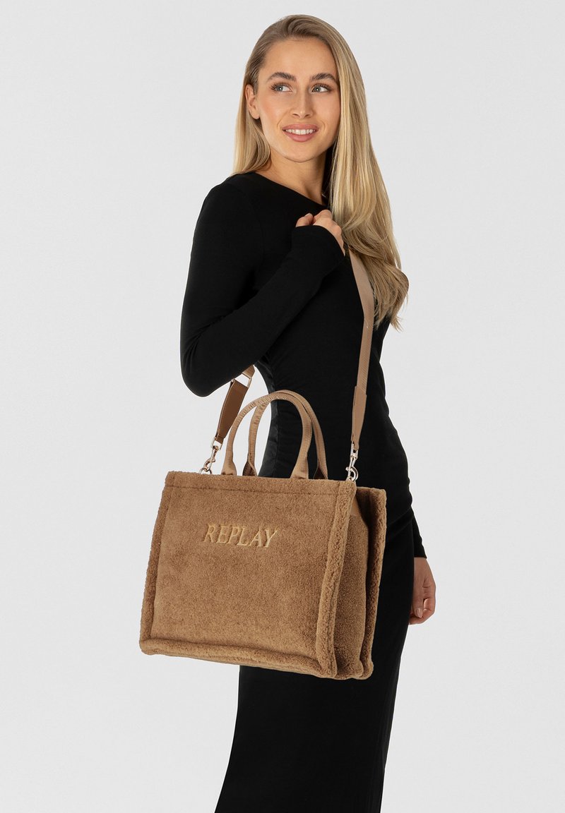 Bruine fleece handtas met een rechthoekige vorm, voorzien van twee handvatten en een afneembare schouderband. Gouden "REPLAY" logo aan de voorkant.