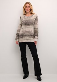 Maglione lavorato a maglia in tonalità neutre presenta un design a strisce testurizzate, scollatura rotonda e maniche lunghe. Abbinato a pantaloni neri a zampa.