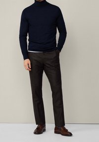 Laivastonsininen pooloneule yhdistettynä tummiin, teksturoituihin housuihin ja ruskeisiin nahkakenkiin. Neuleessa on istuva malli ja pitkät hihat.