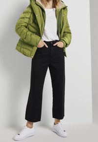 Grøn polstret jakke med hætte, hvid t-shirt, sorte højtaljede vide jeans og hvide sneakers. Har lynlås og trykknaplukning.