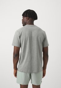 Pelēks īsajiem piedurknēm T-krekls ar apaļu izgriezumu, izgatavots no mīkstas auduma. Tam ir brīva piegriezuma siluets un nedaudz izliekts apakšmalas dizains, valkāts ar gaiši zaļām šortiem.