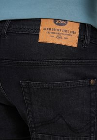 Ciemnoniebieskie dżinsy z skórzaną metką z napisem "Denim Driven Since 1989" oraz wzorem przeszyć na tylnej kieszeni. Miękka tekstura, klasyczny krój.