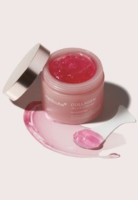 Rosa kollagen jellykräm i en genomskinlig burk med ett silverlock. En liten vit spatel vilar bredvid en gelklump och ett smörj på ytan.